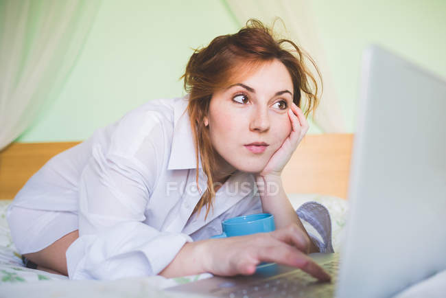 Молода жінка на колінах у ліжку за допомогою ноутбука — стокове фото
