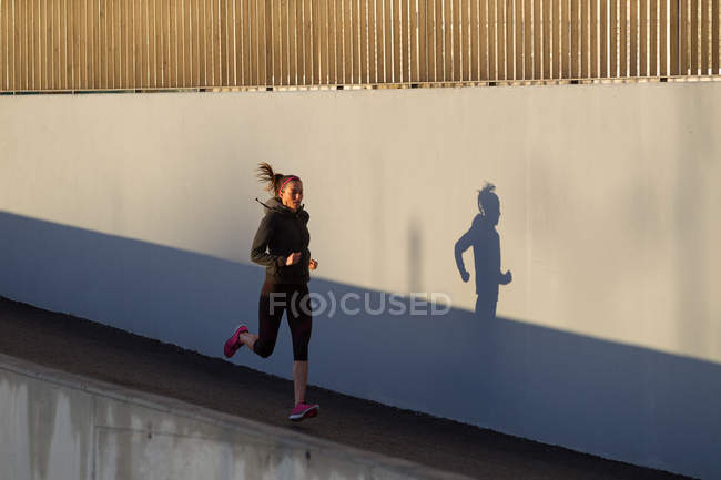 Junge Frau joggt neben Betonmauer — Stockfoto