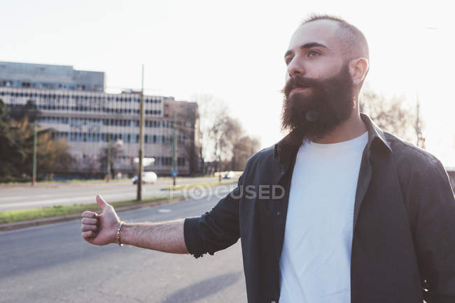 Молодий бородатий чоловік автостопом біля дороги — стокове фото