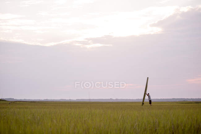 Vista distante do homem que prende a prancha de surf quando estando no campo verde — Fotografia de Stock