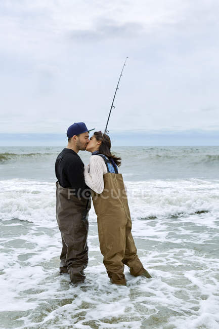 Молодая пара в вадерах целуется во время морской рыбалки — стоковое фото