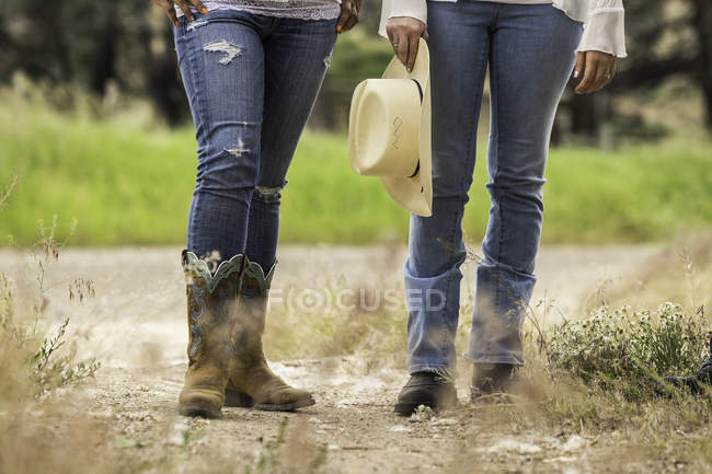 Waist down view of two young women standing on dirt track at ranch, Bridger, Montana, USA — Stock Photo