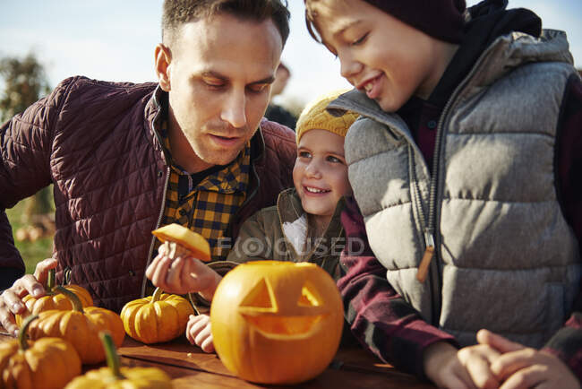 Homem com filho e filha olhando esculpida abóbora halloween em remendo de abóbora — Fotografia de Stock