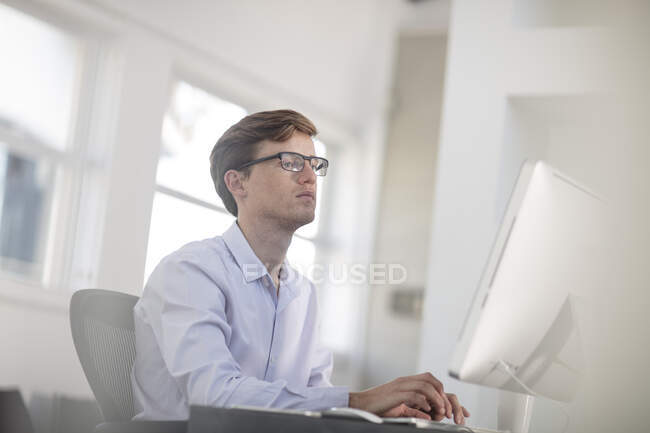 Jovem trabalhador de escritório do sexo masculino digitando no computador desktop — Fotografia de Stock