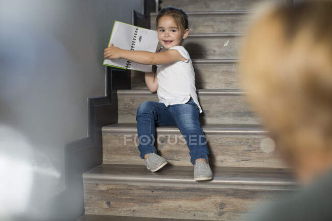Menina nas escadas orgulhosamente mostrando desenhos de lápis de mãe — Fotografia de Stock