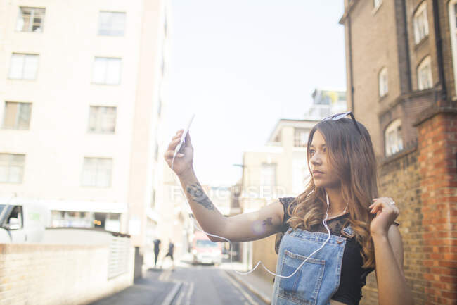 Молодая женщина на улице, делает селфи, используя смартфон — стоковое фото