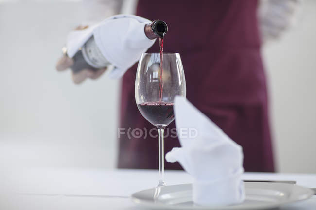 Serveur au restaurant versant un verre de vin rouge, section médiane — Photo de stock