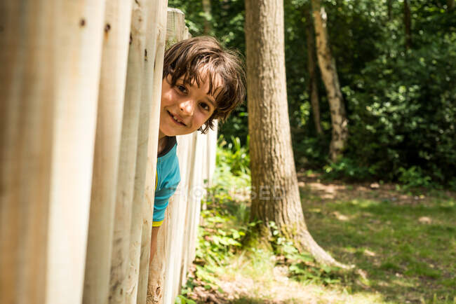 Young boy peering out from wooden fence — Stock Photo