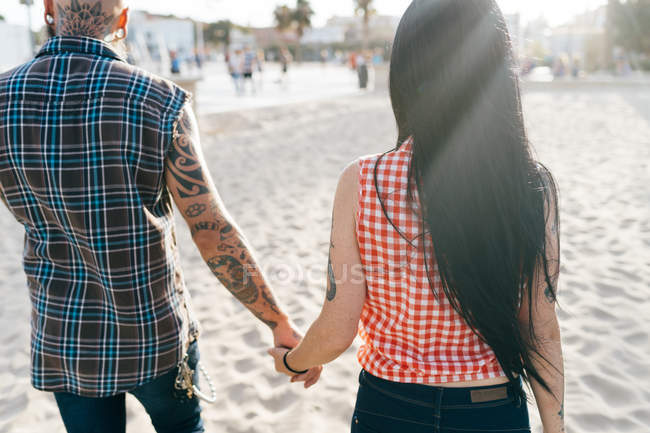 Coppia di hipster tatuati maturi passeggiando sulla spiaggia, vista posteriore, Valencia, Spagna — Foto stock