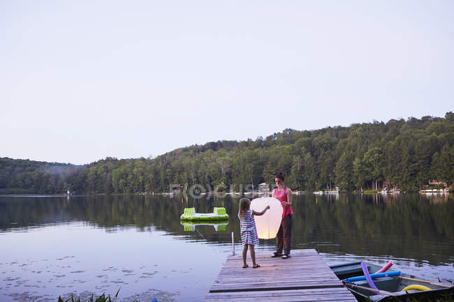 Two girls standing on jetty and releasing sky lantern — Stock Photo