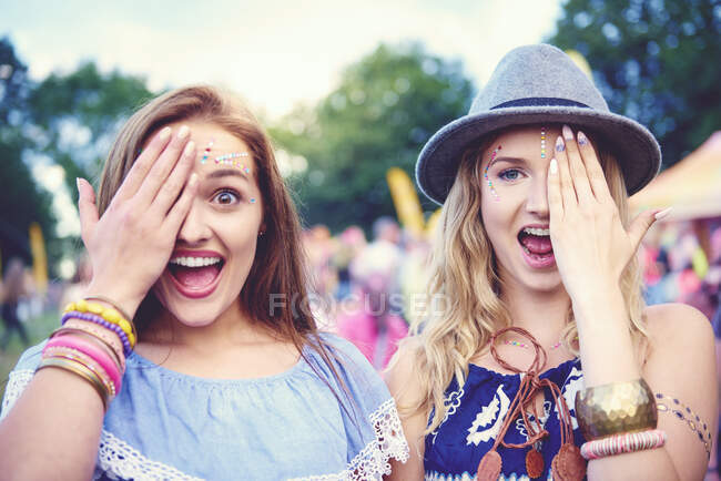 Portrait of two young female friends covering an eye at festival — Stock Photo