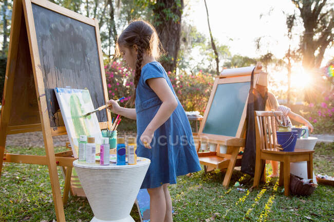 Girl and her sister painting on canvas in garden — Stock Photo