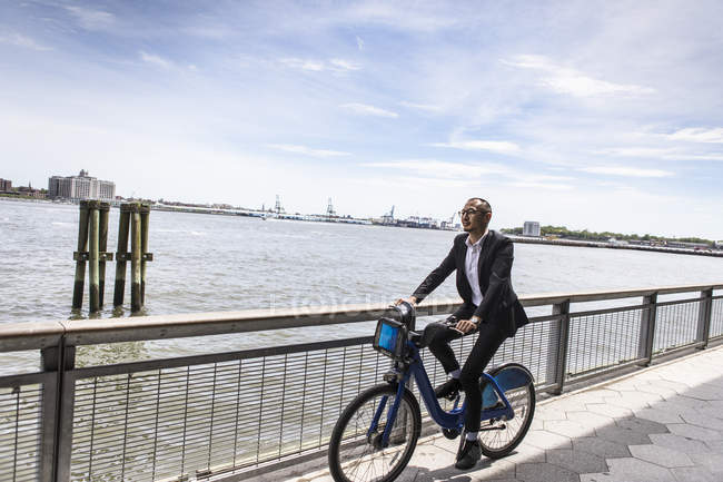 Середній дорослий бізнесмен їде на велосипеді вздовж міської набережної річки — стокове фото