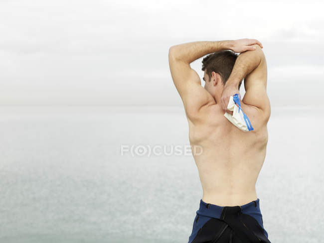 Rear view of bare chested man stretching arms near water, Melbourne, Victoria, Australia, Oceania — Stock Photo