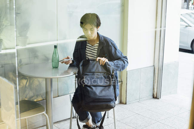 Молодий чоловік тримає смартфон і рюкзак за столом кафе — стокове фото