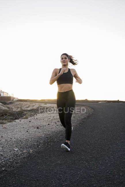 Giovane donna che corre giù su strada rurale — Foto stock