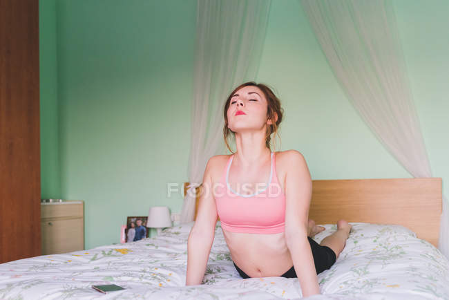 Jeune femme pratiquant le yoga sur le lit — Photo de stock