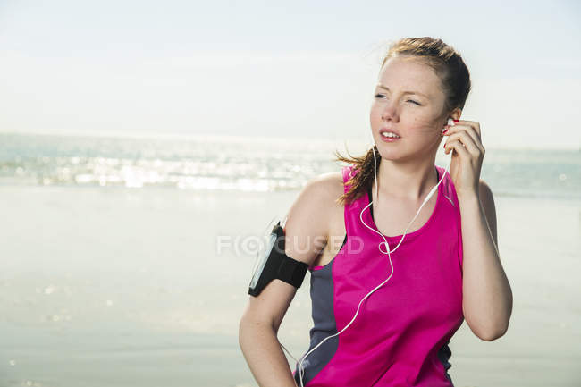 Mujer joven con auriculares mirando hacia la playa - foto de stock
