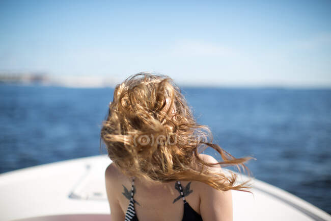 Mujer en barco, pelo soplando en el viento, cubriendo la cara - foto de stock