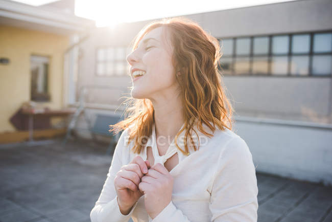 Молода жінка з рудим волоссям сміється на сонячній терасі даху — стокове фото