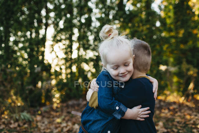 Милая девочка обнимает брата-близнеца в осеннем саду — стоковое фото