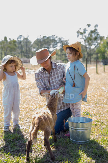 Mutter und zwei Kinder auf Bauernhof, Flasche füttert junge Ziege — Stockfoto