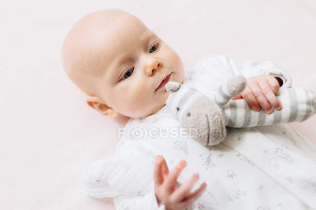 High angle view of Baby girl lying on back holding soft toy — Stock Photo