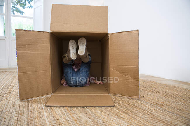 Menino deitado em caixa de papelão com pernas levantadas — Fotografia de Stock