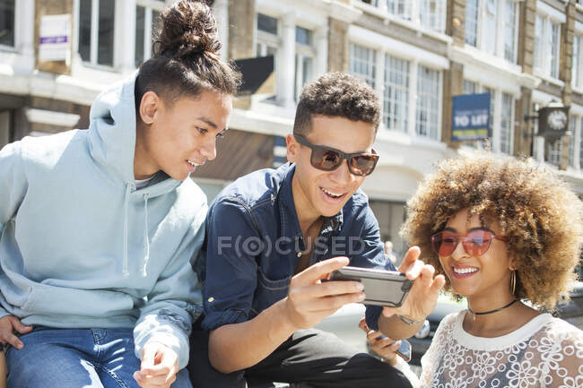 Tres jóvenes amigos al aire libre, mirando el teléfono inteligente - foto de stock
