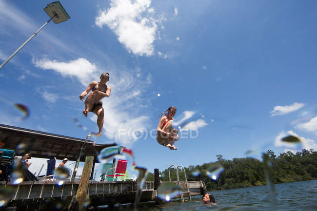 Teenagers jumping into lake, low angle view — Stock Photo