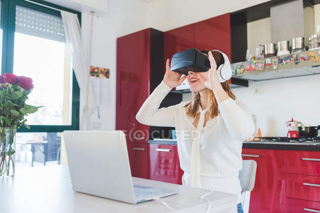 Jovem mulher na mesa da cozinha olhando através de fone de ouvido realidade virtual — Fotografia de Stock