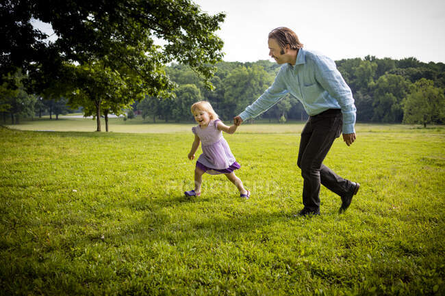 Girl running in rural field with father — Stock Photo