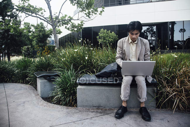 Hombre joven sentado al aire libre y utilizando el ordenador portátil - foto de stock