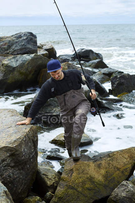 Молодий чоловік рибалка чіпляється за пляжні скелі — стокове фото