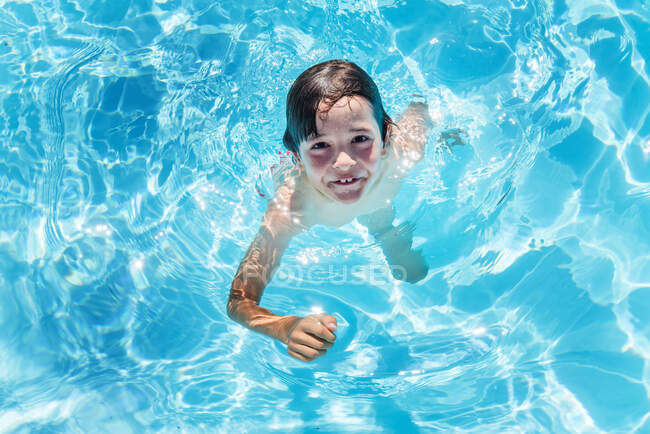 Retrato aéreo de menino pisando a água na piscina ao ar livre iluminada pelo sol — Fotografia de Stock