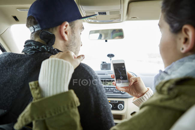 Young couple sitting in car and woman holding smartphone with map on screen — Stock Photo