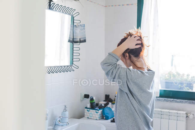 Молода жінка укладає волосся у дзеркало ванної кімнати — стокове фото