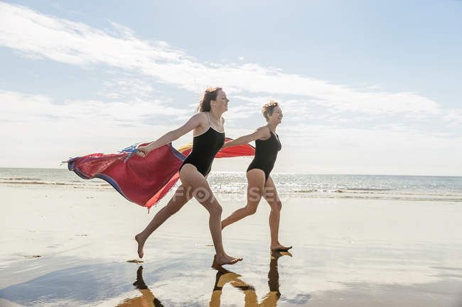 Мати і дочка бігають на пляжі з хустками в повітрі — стокове фото