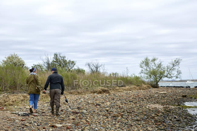 Vista posteriore della giovane coppia di pescatori passeggiando sulla spiaggia di ghiaia — Foto stock