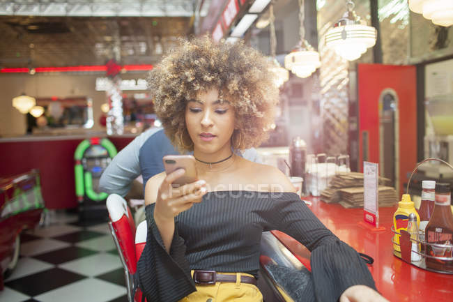 Vista frontal da mulher jovem sentada no restaurante e usando smartphone — Fotografia de Stock