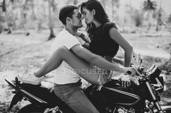 Вид сбоку на молодую пару, обнимающую мотоцикл — стоковое фото