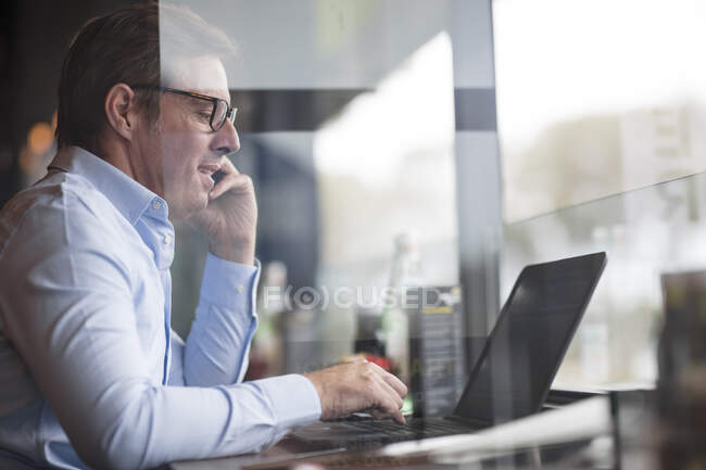 Homme dans le café en utilisant ordinateur portable et smartphone — Photo de stock