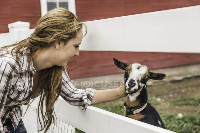 Young woman petting goat at ranch fence, Bridger, Montana, USA — Stock Photo