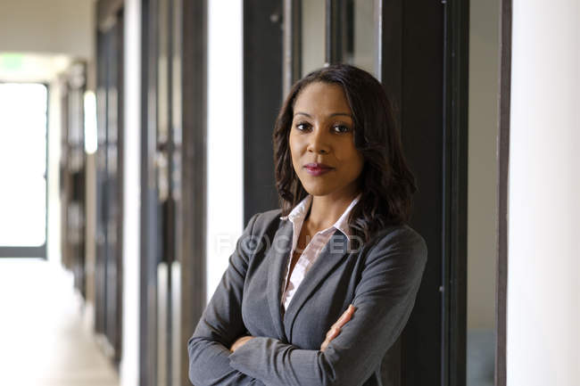 Portrait of businesswoman in office hallway, arms folded, serious expression — Stock Photo