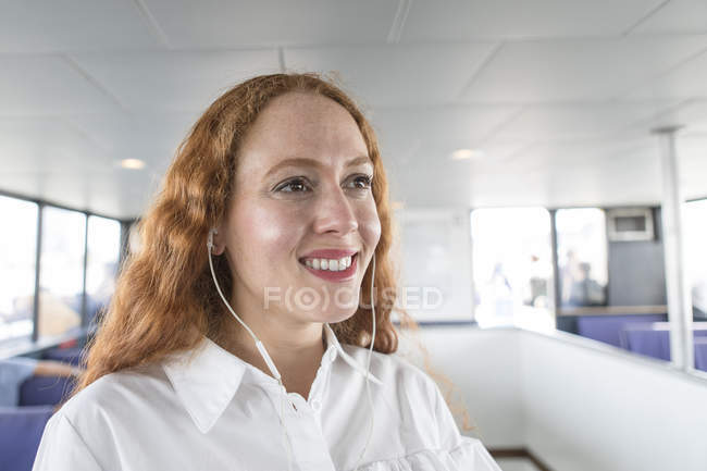 Улыбающаяся женщина слушает музыку в наушниках на пассажирском пароме — стоковое фото