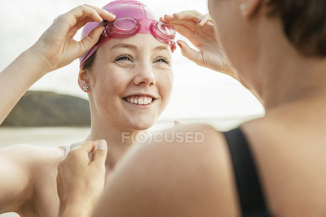 Madre e hija ajustando gafas de natación en la playa - foto de stock