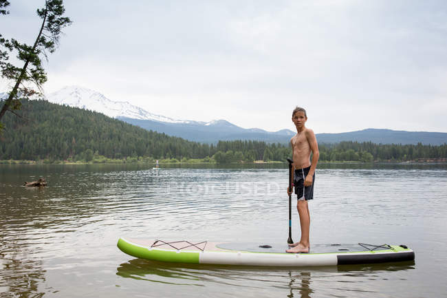 Vue lointaine du garçon adolescent sur la planche à pagaie contre la forêt verte — Photo de stock