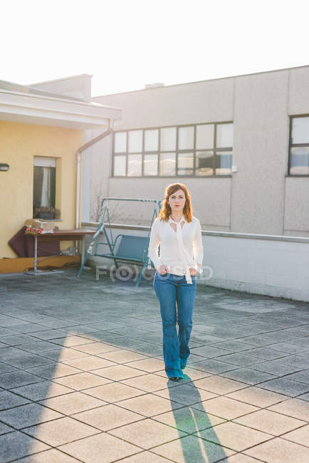 Портрет молодой женщины, идущей по террасе на крыше с руками в карманах — стоковое фото