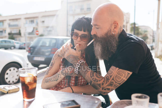 Зрелая пара хипстеров закуривает сигарету в кафе на тротуаре, Валенсия, Испания — стоковое фото