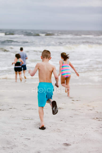 Hombre y niños corriendo hacia el mar desde la playa, vista trasera, Isla Delfín, Alabama, EE.UU. - foto de stock